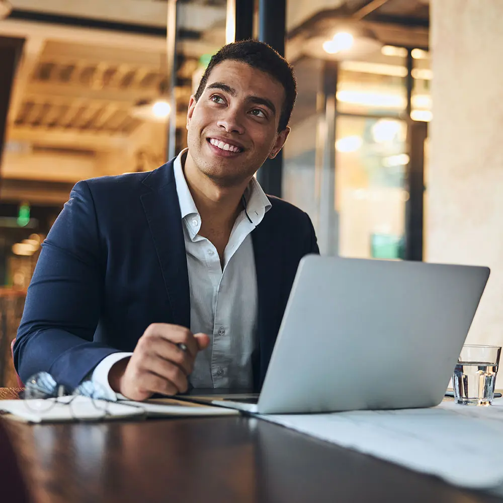 young man in a suit sitting at a table with a laptop
