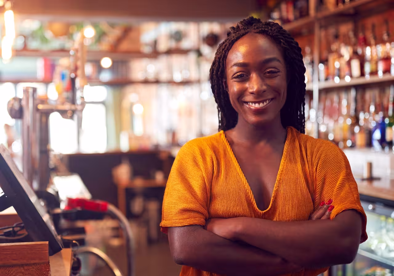 young woman in a dress stands smiling at the till of a bar